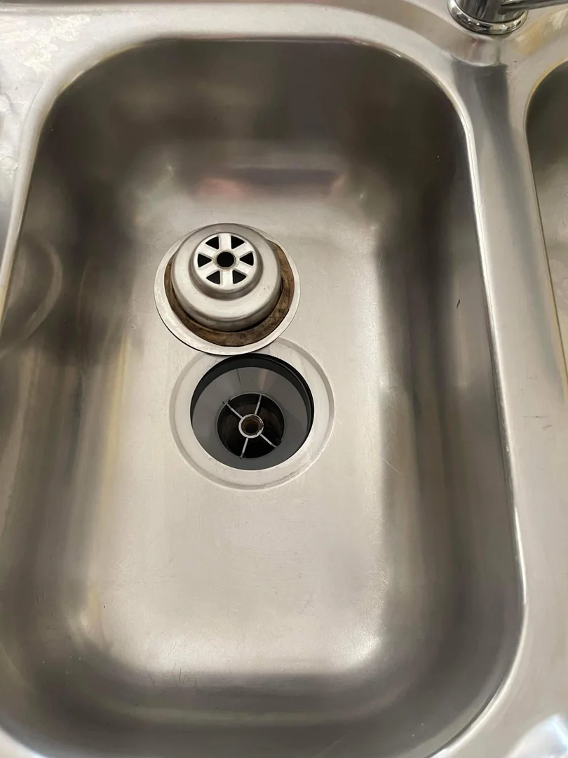Same sink drain after deep cleaning — strainer and opening polished and shiny silver.