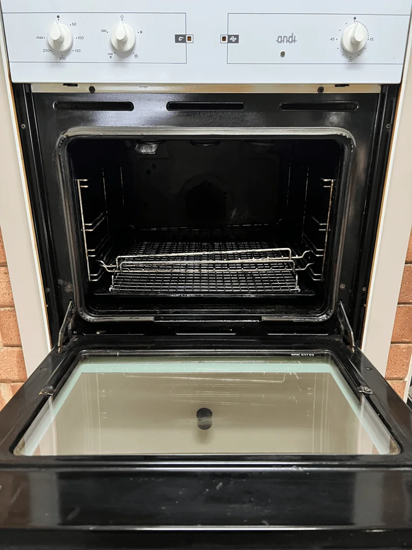 Same oven after cleaning — interior walls are uniform black, glass door clear and reflective, racks back in place.