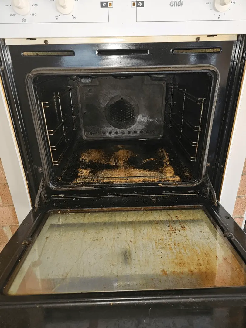 Oven interior coated in thick, baked-on black and brown grease with a film-covered glass door before cleaning.
