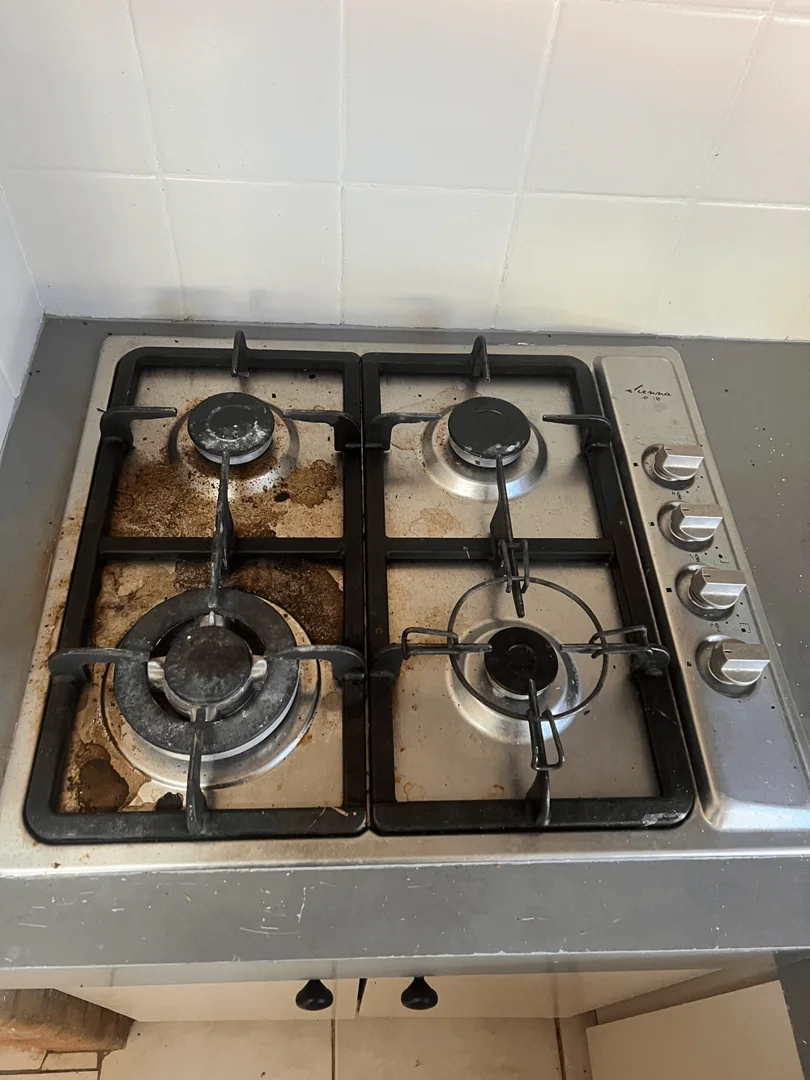 Stainless steel gas stovetop heavily soiled with burnt-on grease and food spills around the burners before cleaning.
