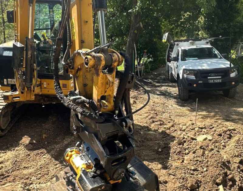 Hydraulic hose being fixed on a yellow digger beside a white truck